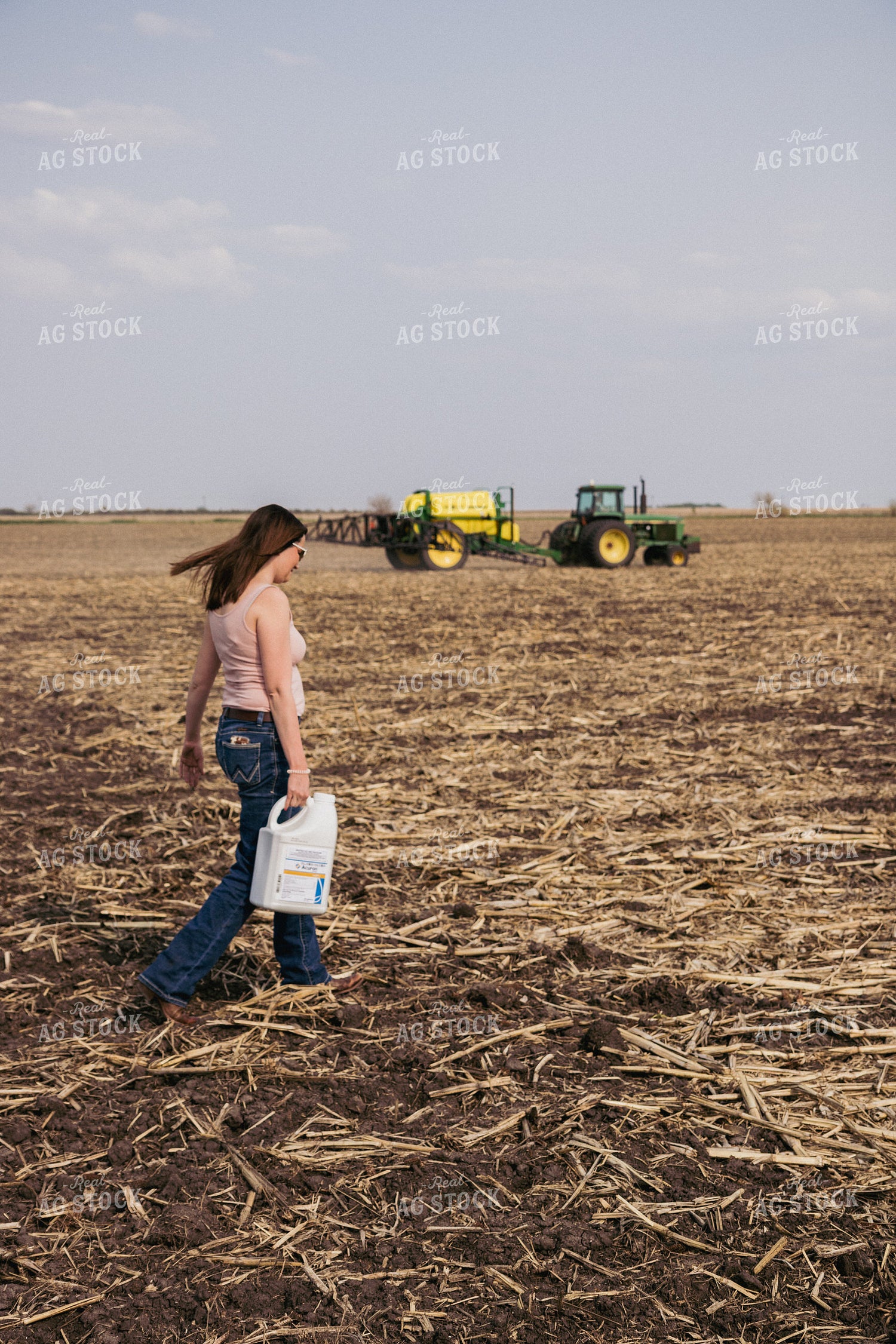 Female Farmer Carries Pesticide Concentrate in Field with Sprayer in Background 67285