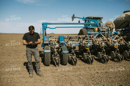 Farmer Looking at Phone in Field with Planter in Background 4126