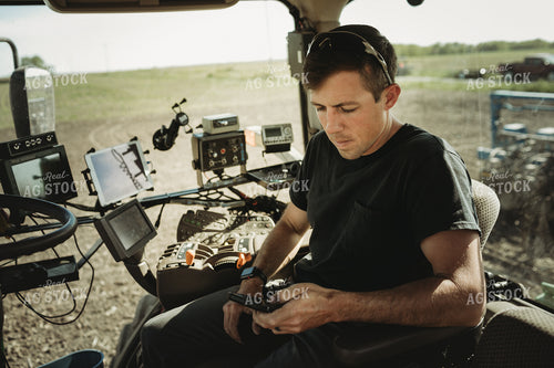 Farmer Looking at Phone in Tractor Cab 4120