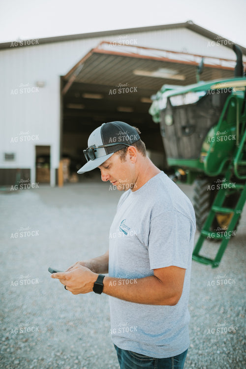 Farmer Looking at Phone with Sprayer in Background 6255