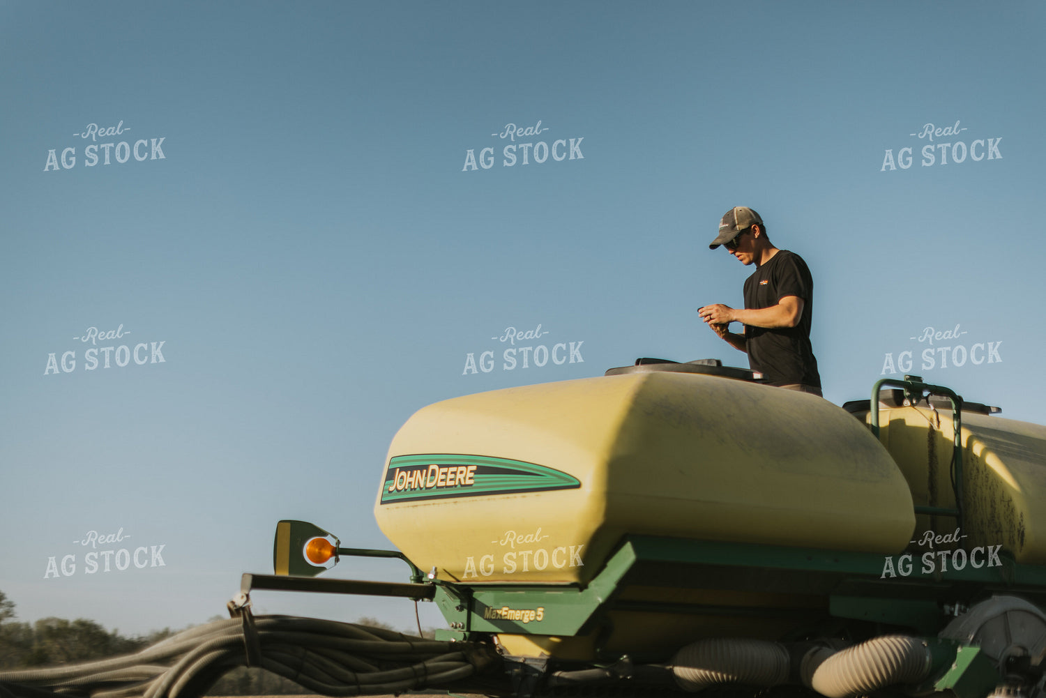 Young Farmer Looks at Phone While Standing on Planter 7655