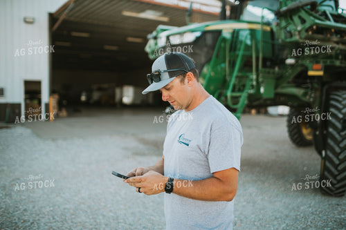 Farmer Looking at Phone with Sprayer in Background 6254