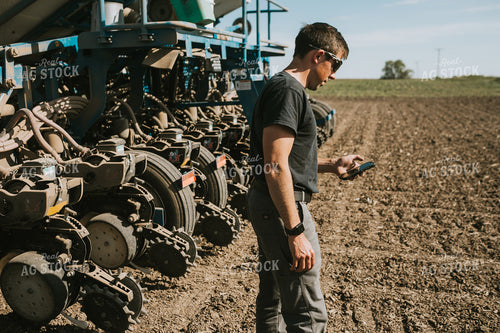 Farmer Looking at Phone in Field with Planter in Background 4125