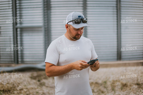 Farmer Looking at Phone by Grain Bin 8761