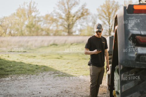 Young Farmer Looks at Phone Next to Tractor 7645