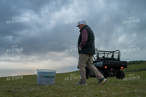 Man Inspects Farming Equipment in Scenic Open Grassland under Overcast Skies 65342