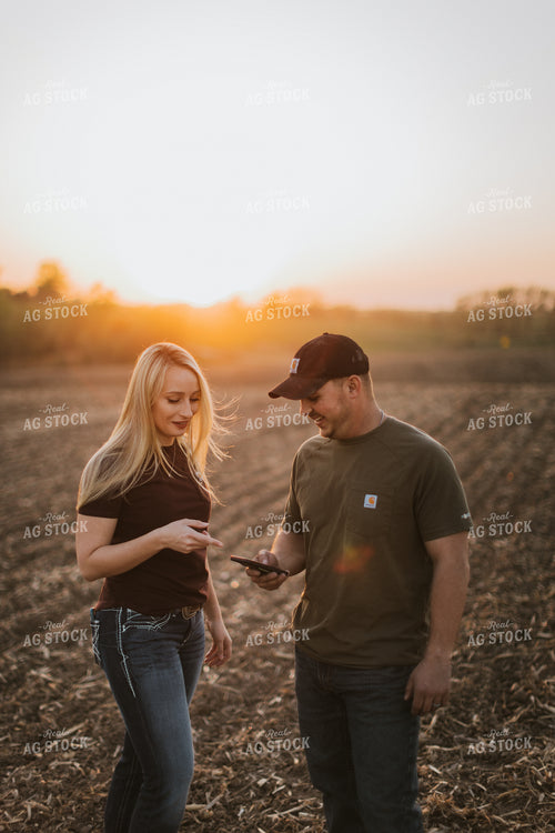Young Couple Look at Phone in Field at Sunset 7729
