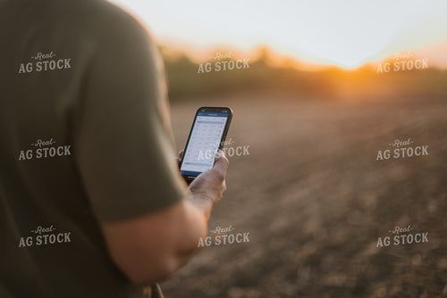 Young Farmer Looks at Phone in Field at Sunset 7734