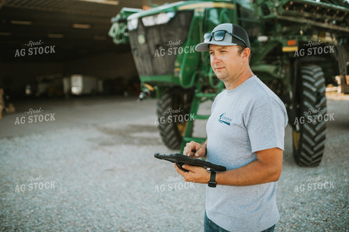 Farmer Looking at iPad with Sprayer in Background 6249