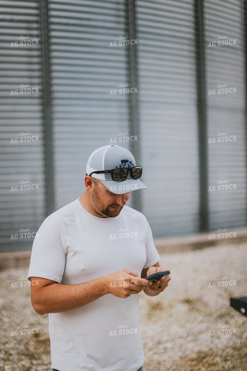 Farmer Looking at Phone by Grain Bin 8760