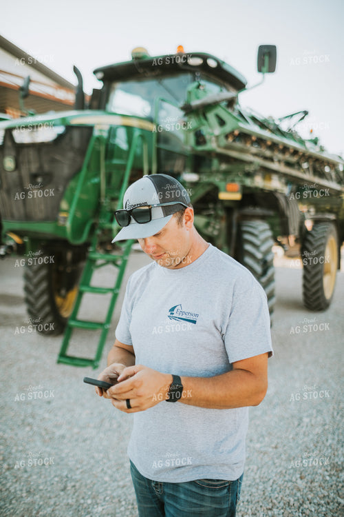 Farmer Looking at Phone with Sprayer in Background 6251