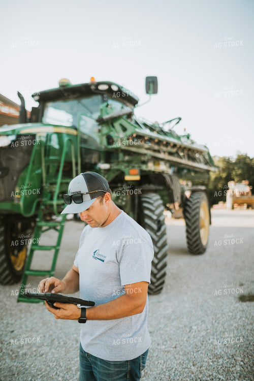 Farmer Looking at iPad with Sprayer in Background 6246