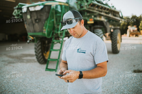 Farmer Looking at Phone with Sprayer in Background 6253