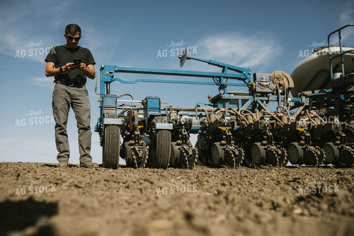 Farmer Looking at Phone in Field with Planter in Background 4127