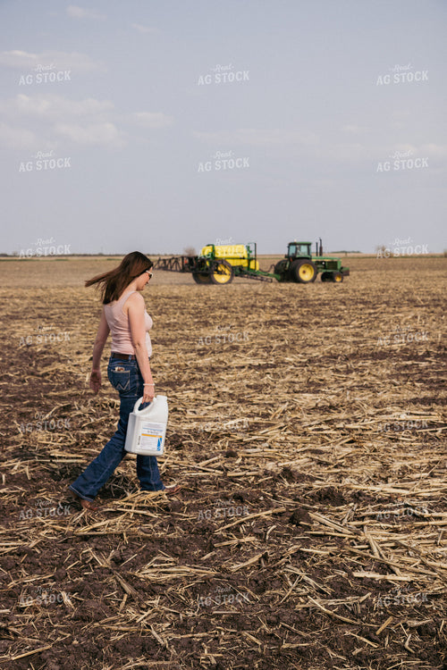 Female Farmer Carries Pesticide Concentrate in Field with Sprayer in Background 67285