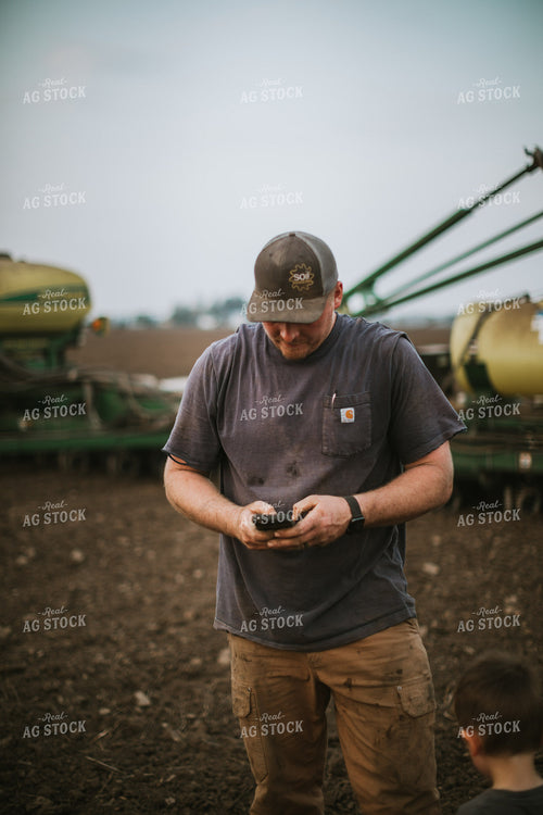 Farmer Looking at Phone in Field with Planter 5671