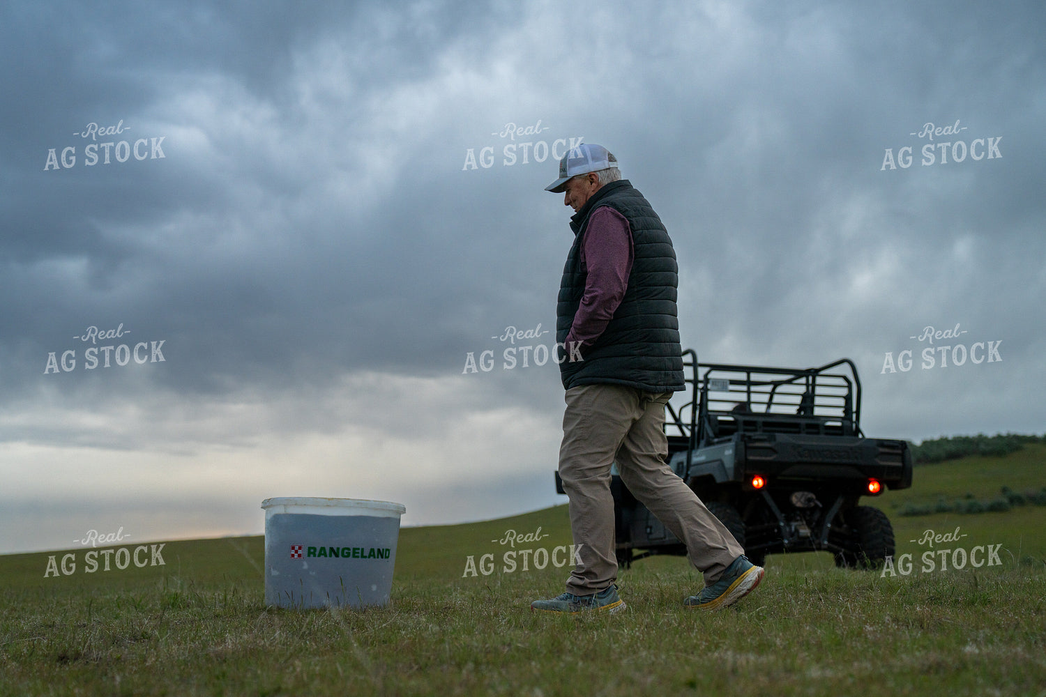 Man Inspects Farming Equipment in Scenic Open Grassland under Overcast Skies 65286