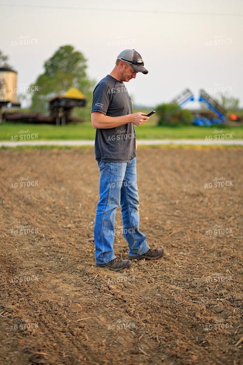 Farmer Looks at Phone in Field 93211