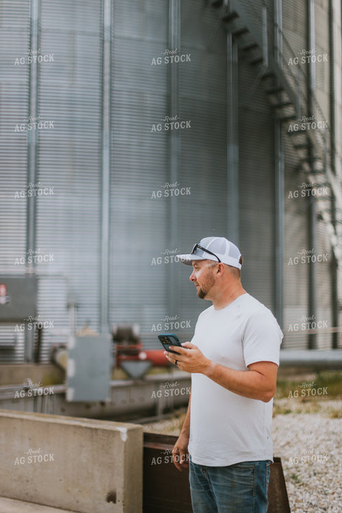 Farmer Looking at Phone by Grain Bin 8767
