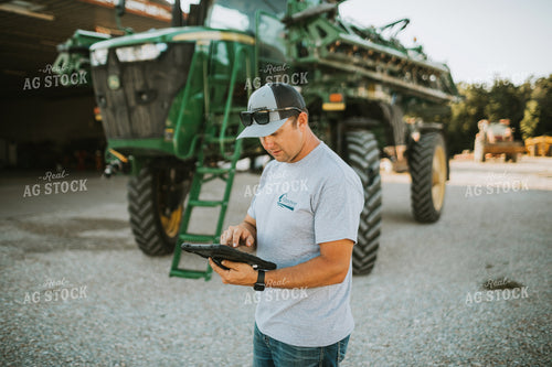 Farmer Looking at iPad with Sprayer in Background 6247