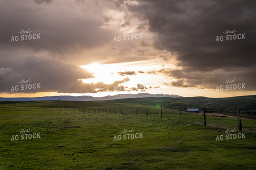 Scenic Sunset Over Rolling Hills with Distant Cattle Ranch and Fenced Fields 65228