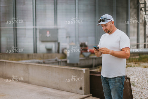 Farmer Looking at Phone by Grain Bin 8765