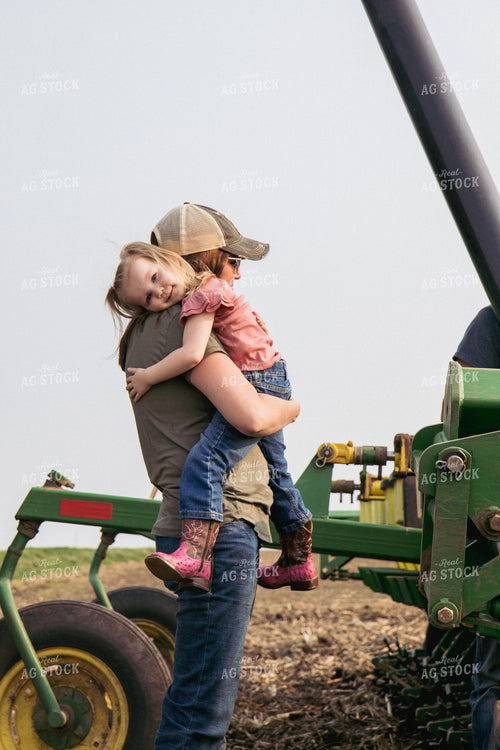 Female Farmer and Daughter Embrace by Planter in Field 67312