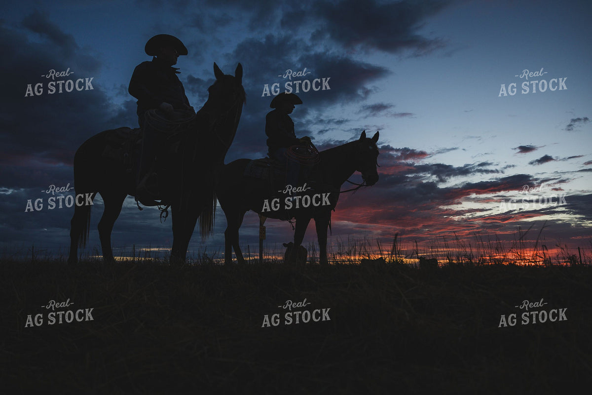 Two Cowboys on Horseback Silhouetted Against a Dramatic Sunset Sky 404036